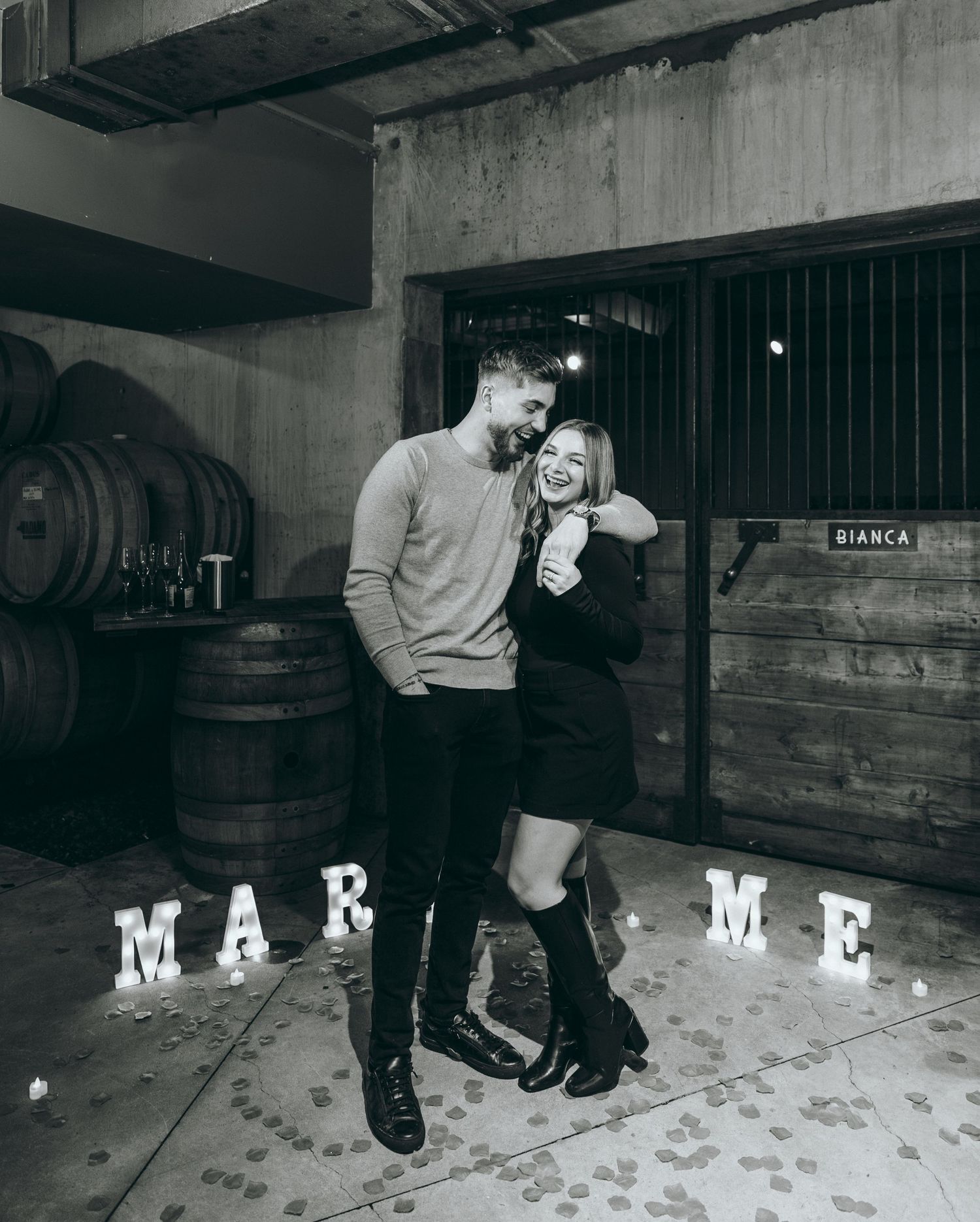 Marriage proposal scene in rustic venue with decorative letters spelling out proposal.