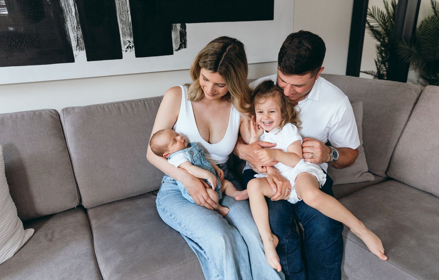 A family relaxes together on a gray sectional sofa in a modern living room.
