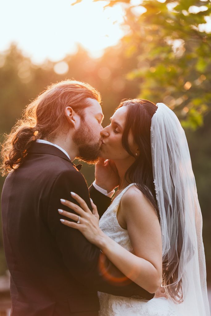 Romantic wedding couple sharing a tender kiss at sunset with golden bokeh lighting in the background.