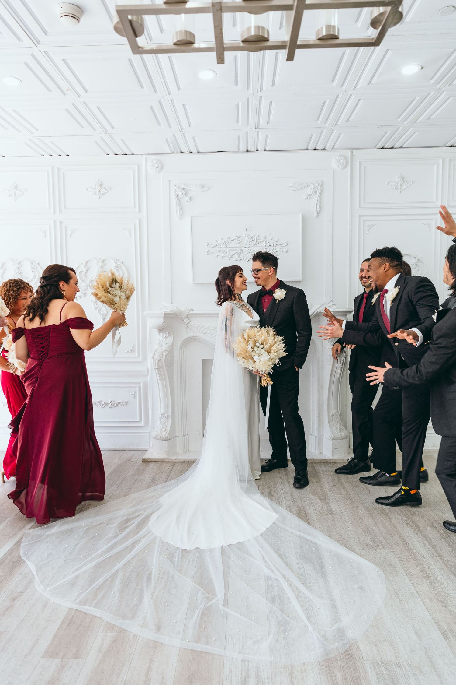 Wedding party celebrating around the couple in an elegant white room with ornate details.