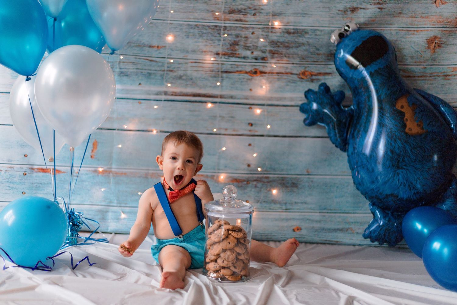 Cookie Monster themed photo setup with blue balloons and rustic wooden background.