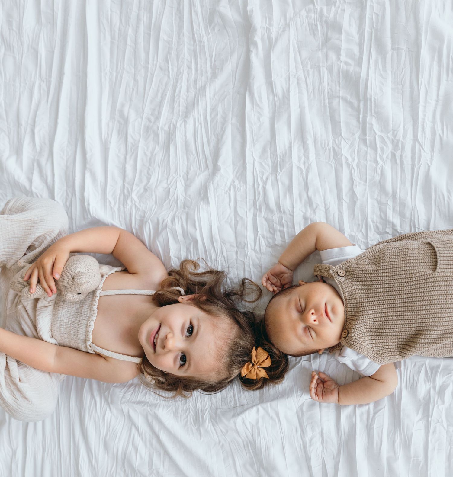 Two children rest side by side on white bedding wearing coordinating outfits.