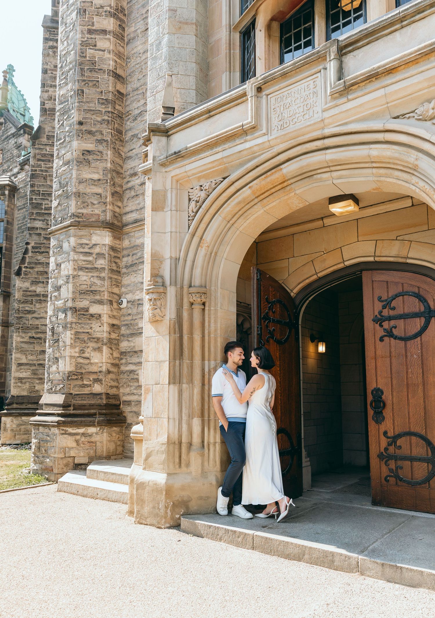 Loving couple shares tender moment under gothic stone archway of historic building.