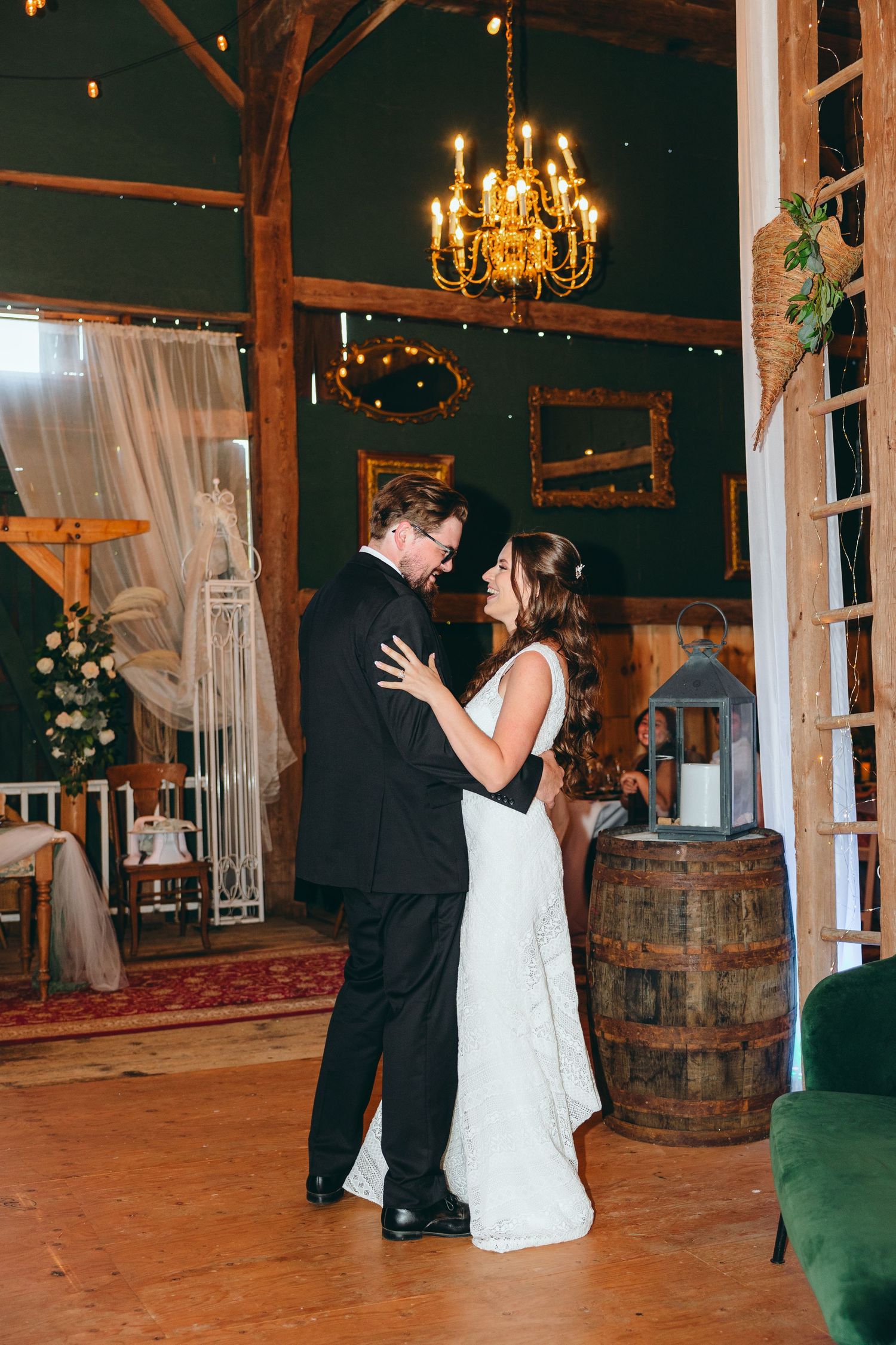 Couple shares their first dance in rustic barn venue with barrel decor and chandeliers.