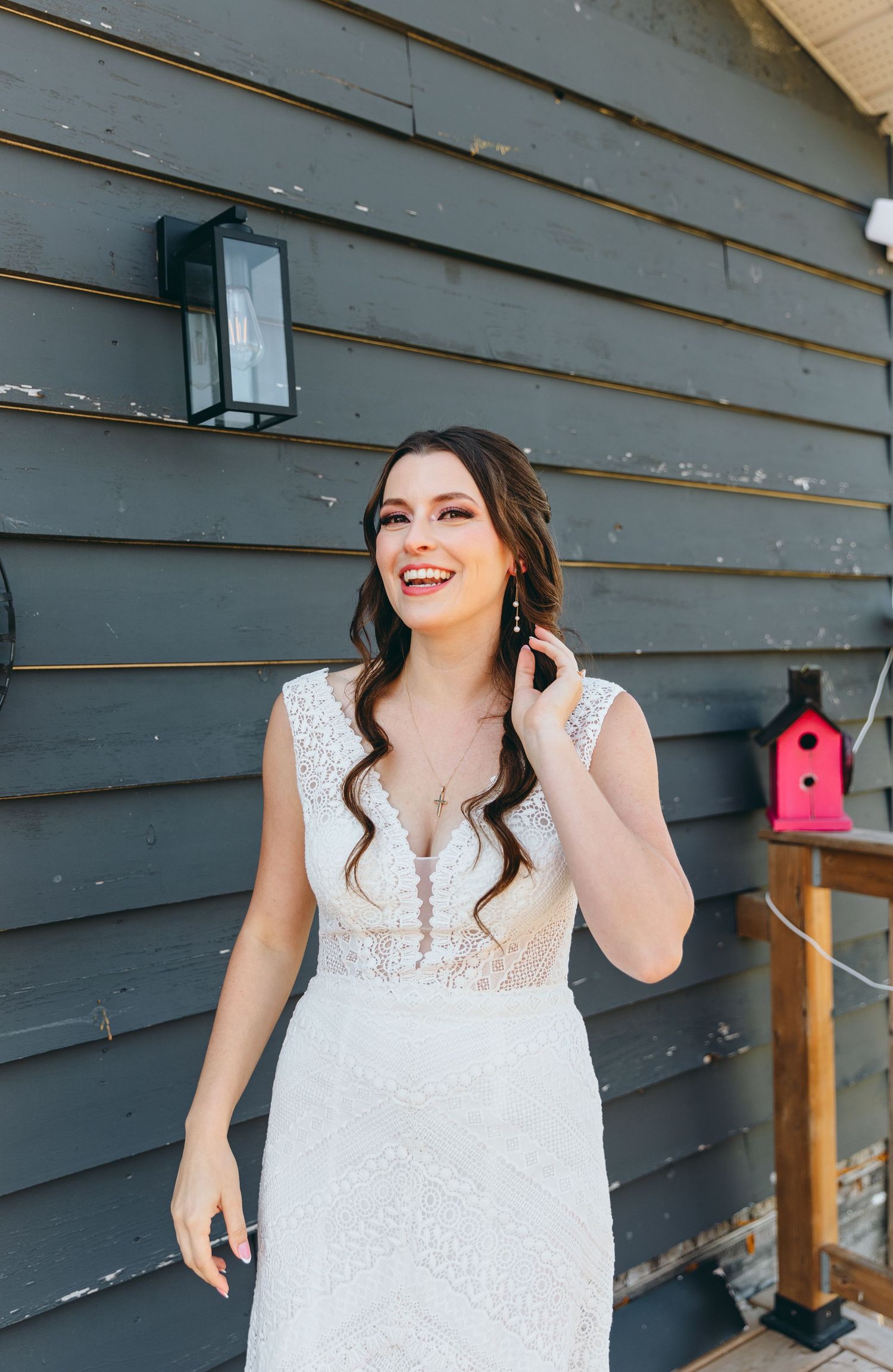 A white lace wedding dress photographed against a gray wooden wall on a porch.