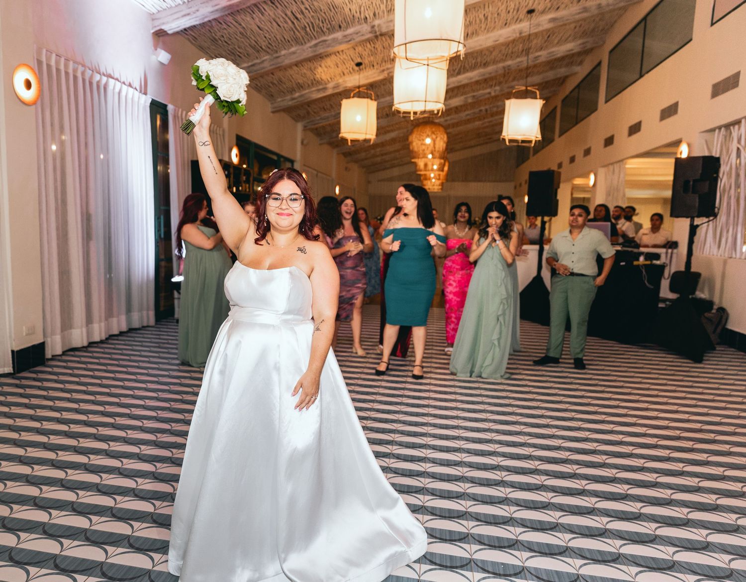 A person in a white wedding gown celebrates on a geometric patterned dance floor.