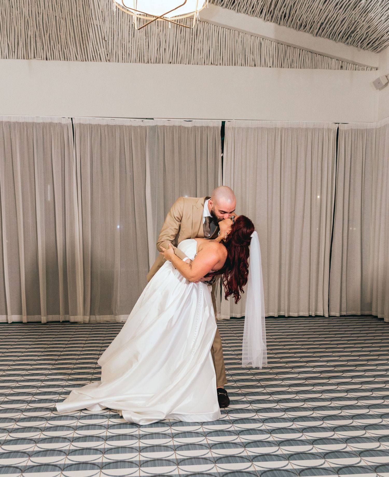 Elegant dance dip on black and white patterned floor during wedding reception.