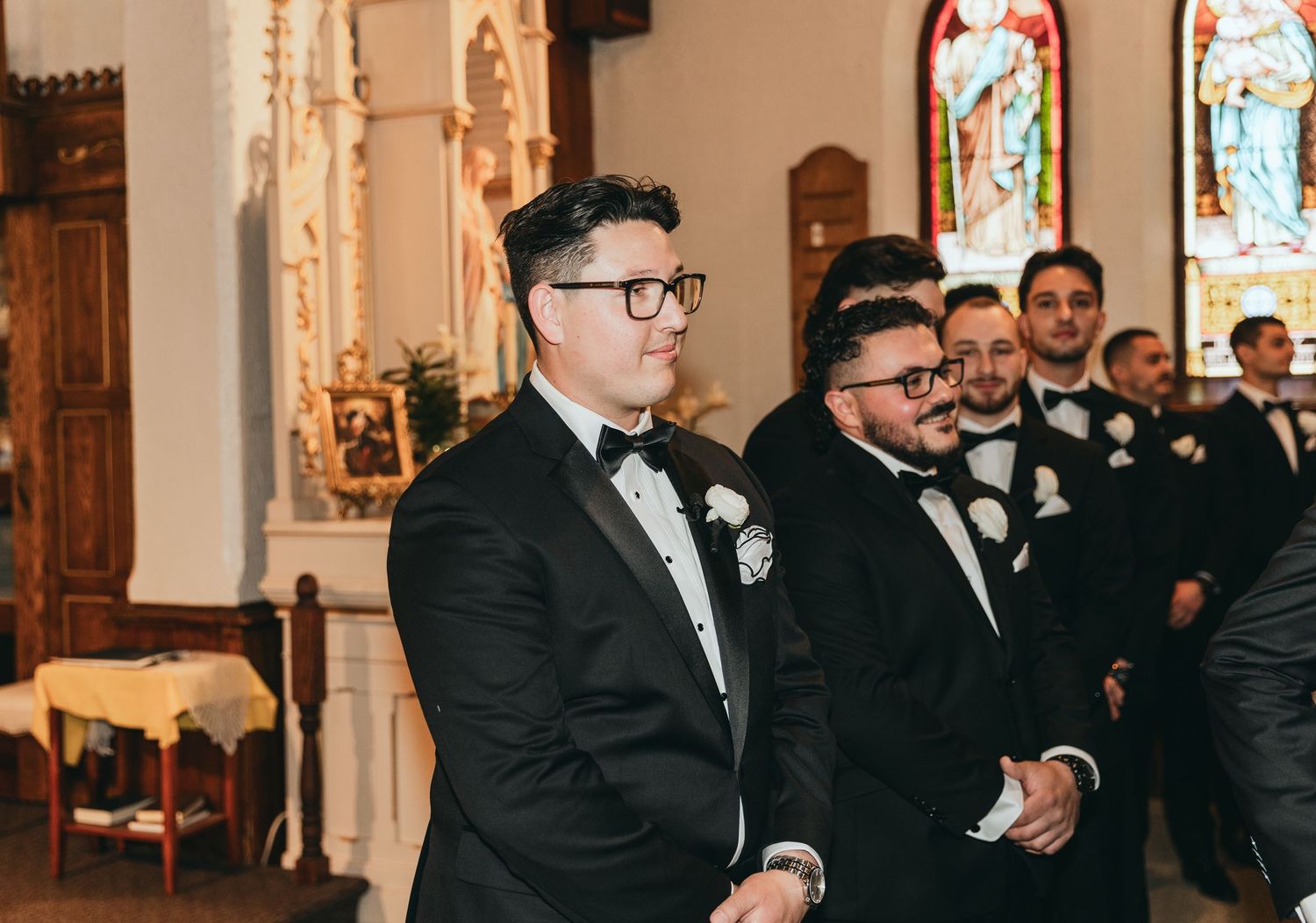 Wedding party members in formal attire gathered inside ornate church interior.