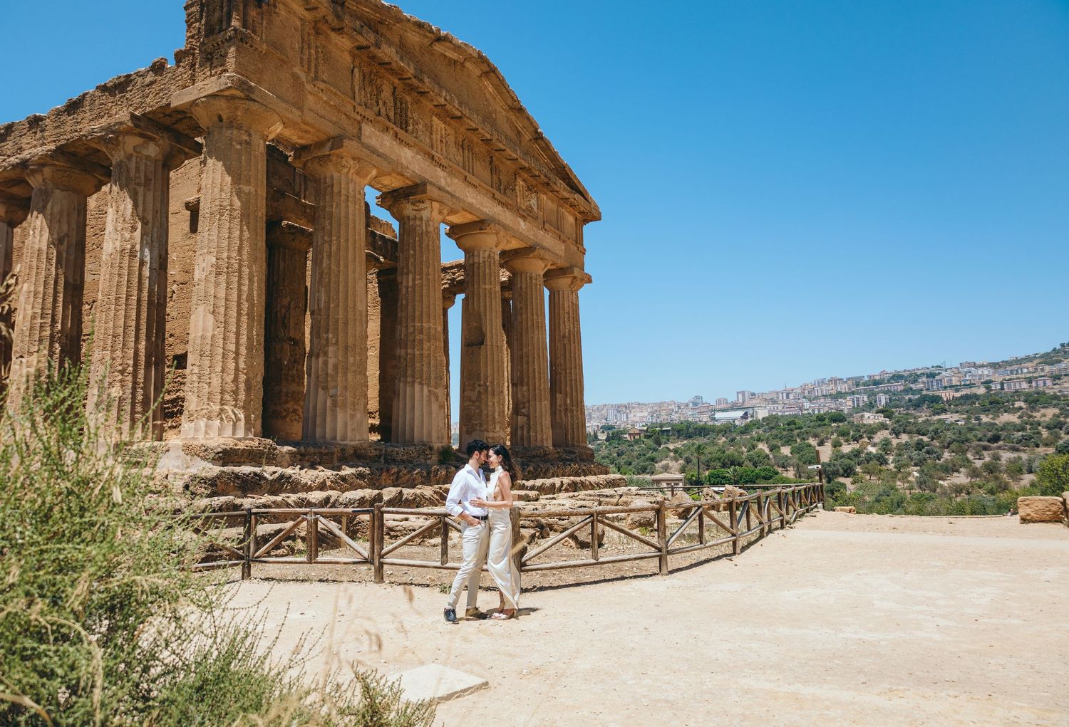 Ancient Greek temple ruins with Doric columns stand against bright blue sky in panoramic view.