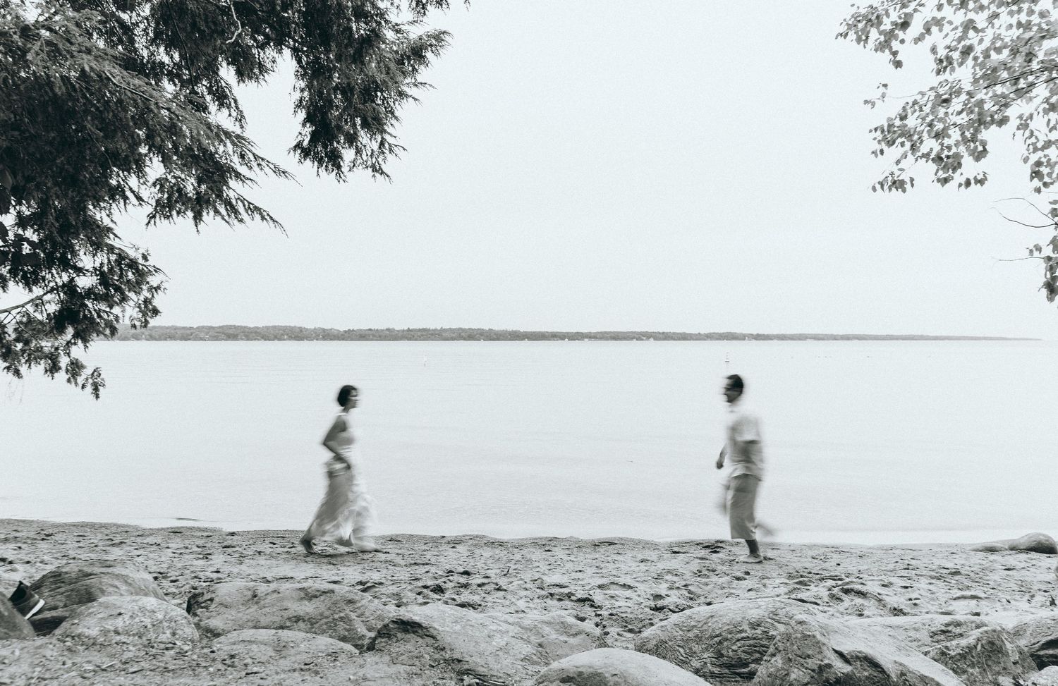 Black and white photo of two people walking on rocky shoreline.