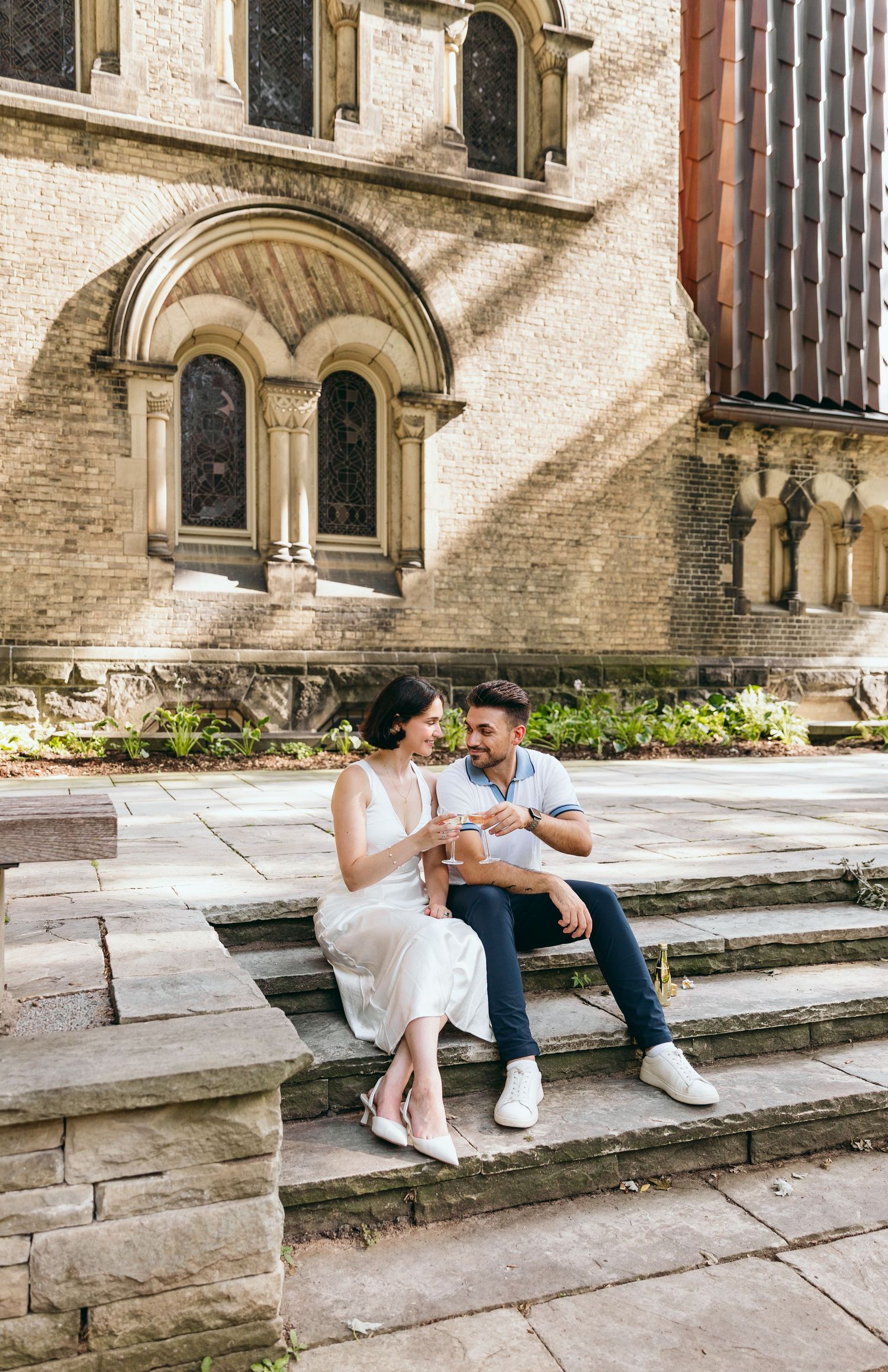 A couple sits on stone steps near a Gothic church window.