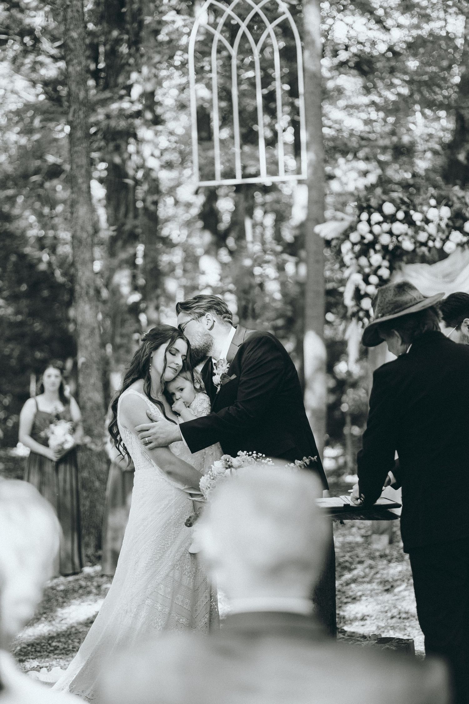 Black and white wedding ceremony photos in a wooded setting with an arched backdrop.