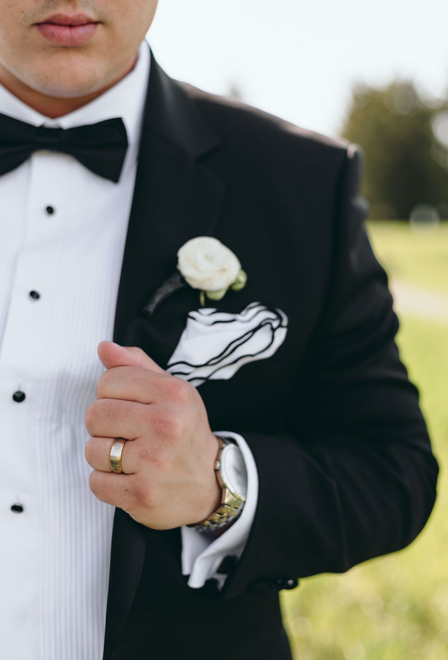 Close-up of groom's classic black tuxedo with white boutonniere and bow tie.