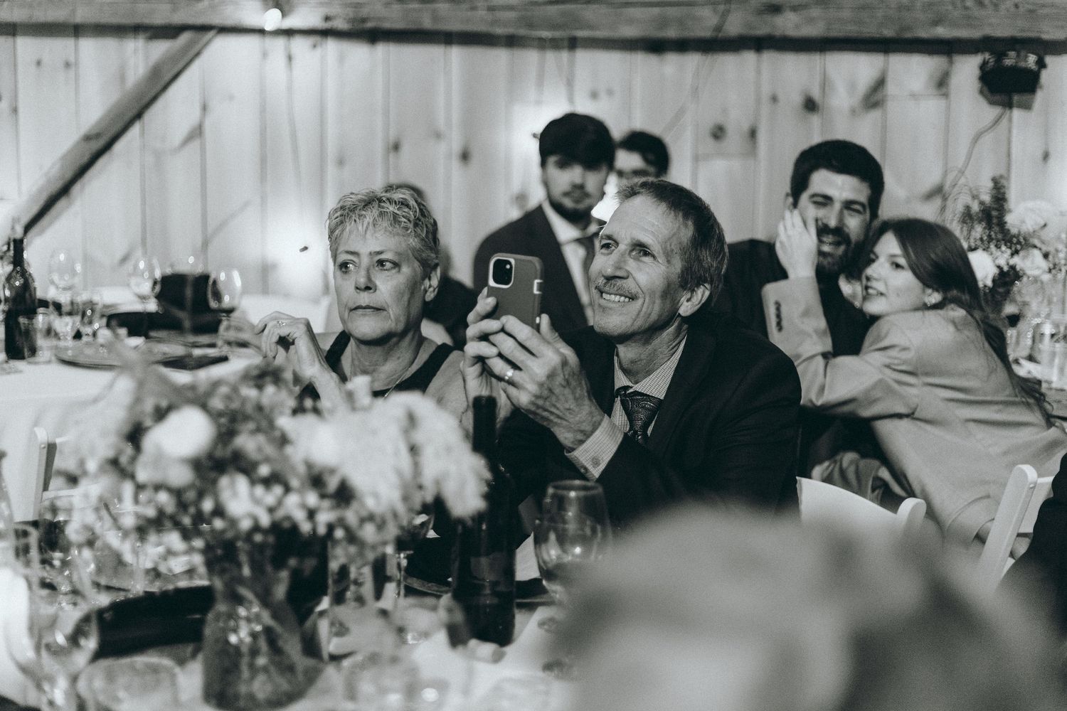 Black and white photo of wedding guests enjoying conversation at reception tables.