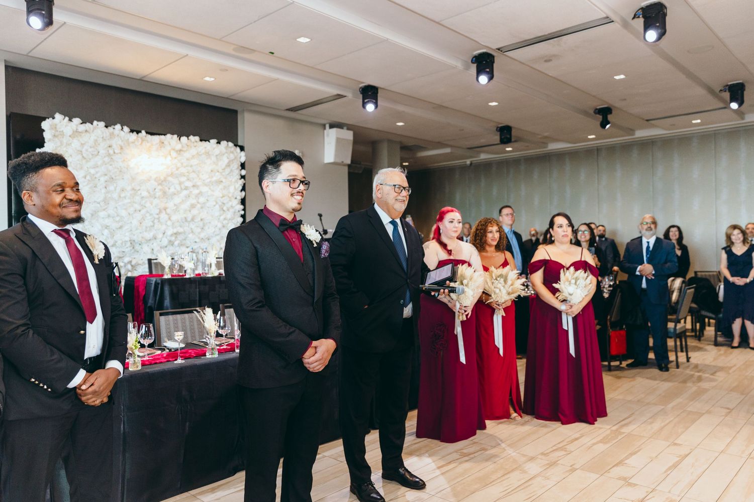 Wedding party members in burgundy dresses and dark suits posing in a bright modern venue.