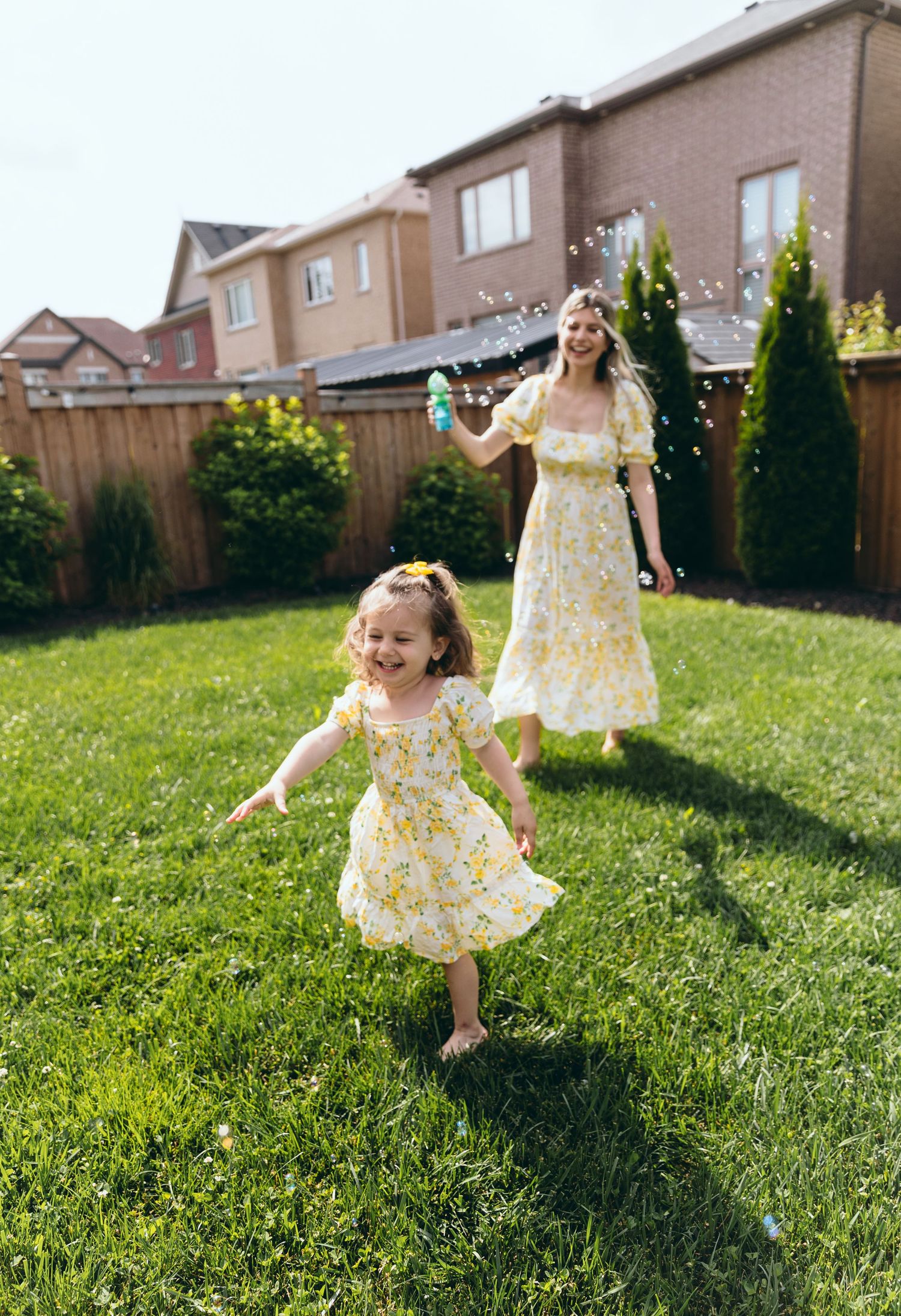 Young child in a floral dress twirling and playing in a sunny backyard with green grass.