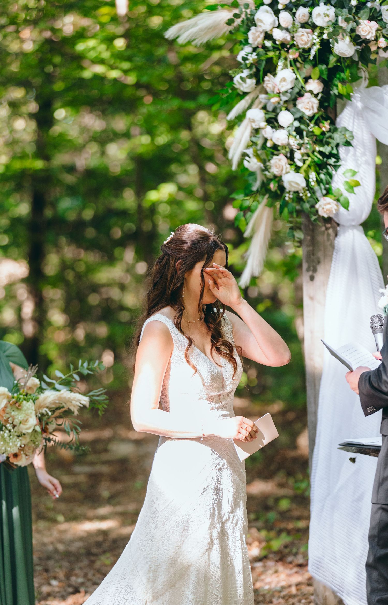 Wedding ceremony under floral arch with white roses in a lush forest setting.