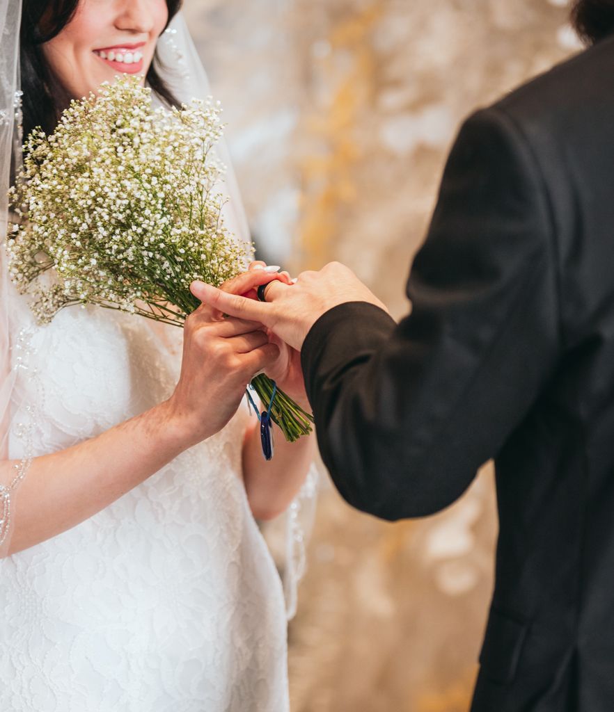 Close-up of hands exchanging rings with a delicate baby's breath bouquet.
