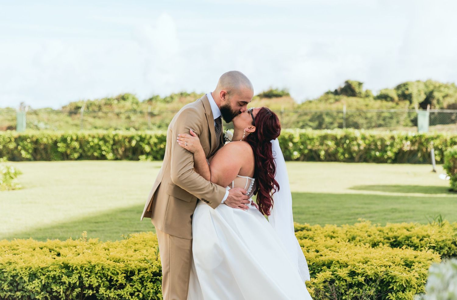 Romantic wedding couple embraces on grassy lawn during sunset.