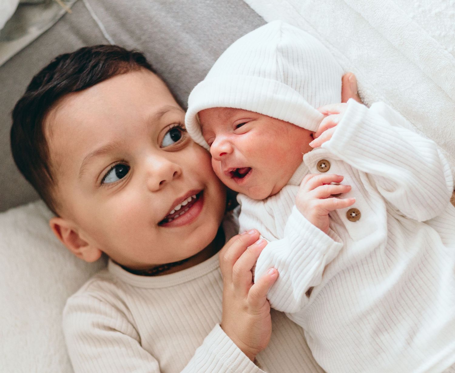 Close-up series of baby in white ribbed outfit lying on white surface.