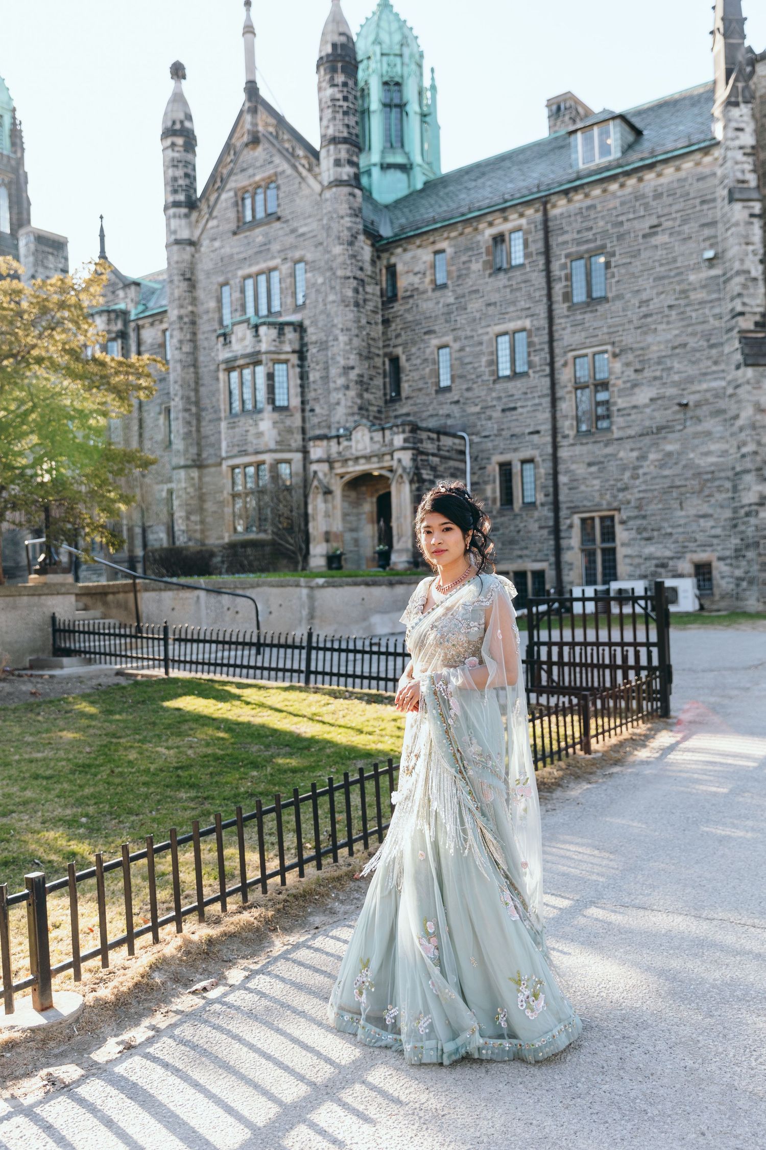 A person in a light blue traditional dress poses in front of a gothic stone building.