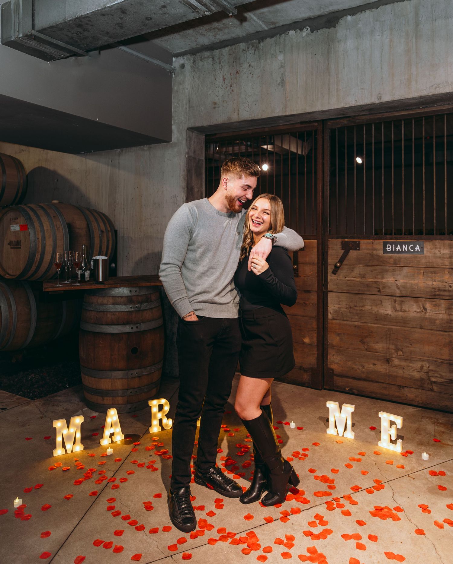 A romantic proposal in a wine cellar with illuminated letters spelling MARRY ME.