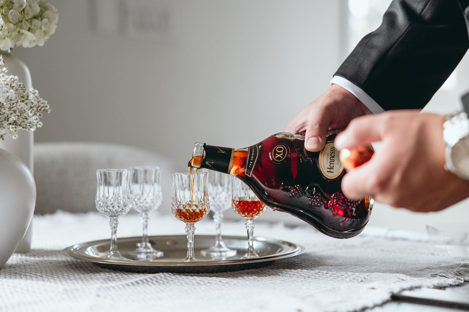 Hands pouring drinks into crystal glasses on an elegant white tablecloth.