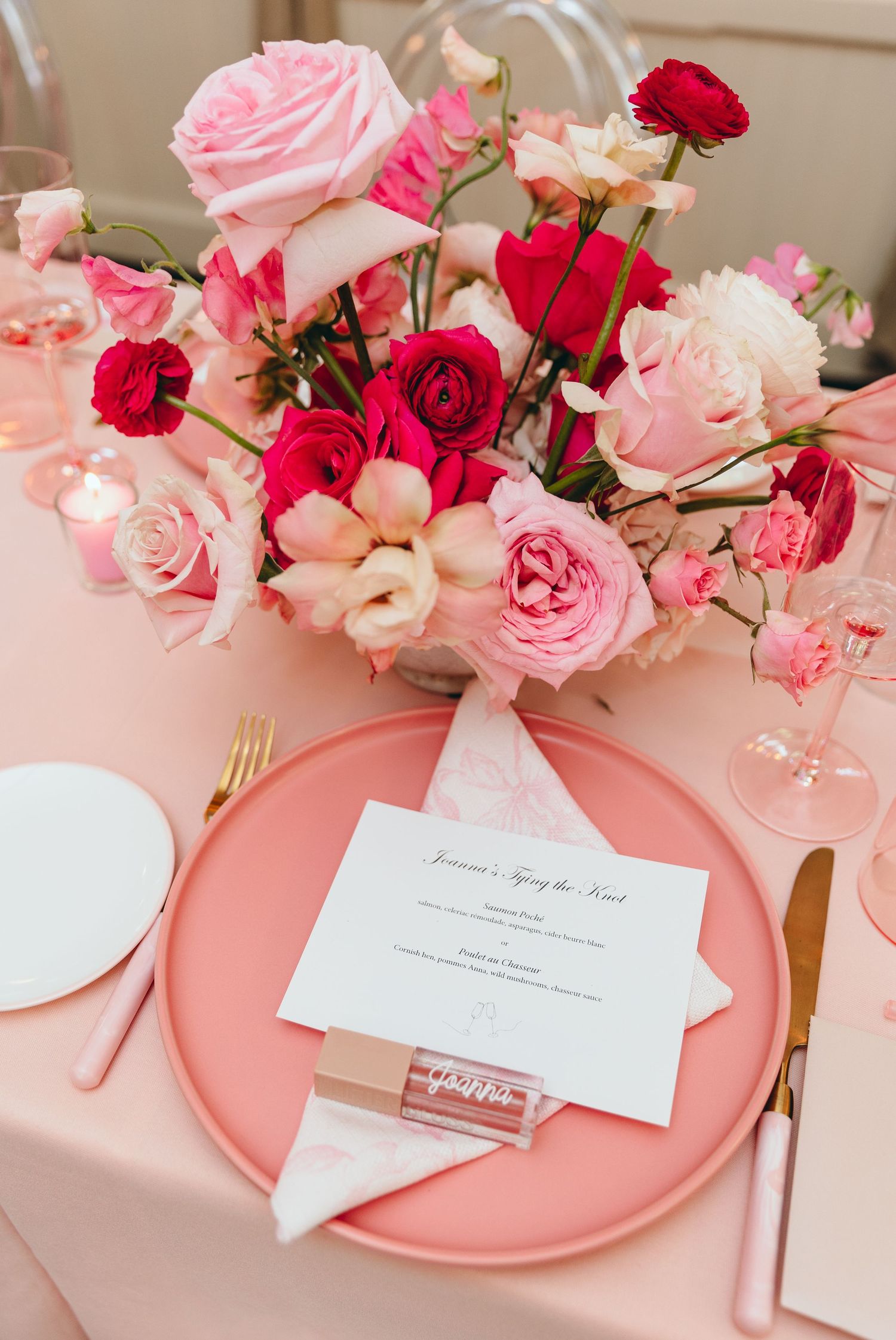 Elegant pink and red roses arranged with place cards on coral-colored charger plates for a romantic table setting.