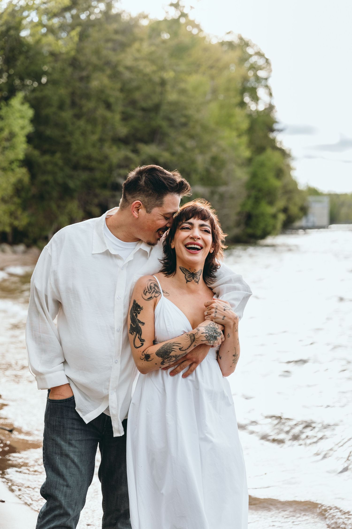 A couple shares joyful moments together on a beach in white outfits.