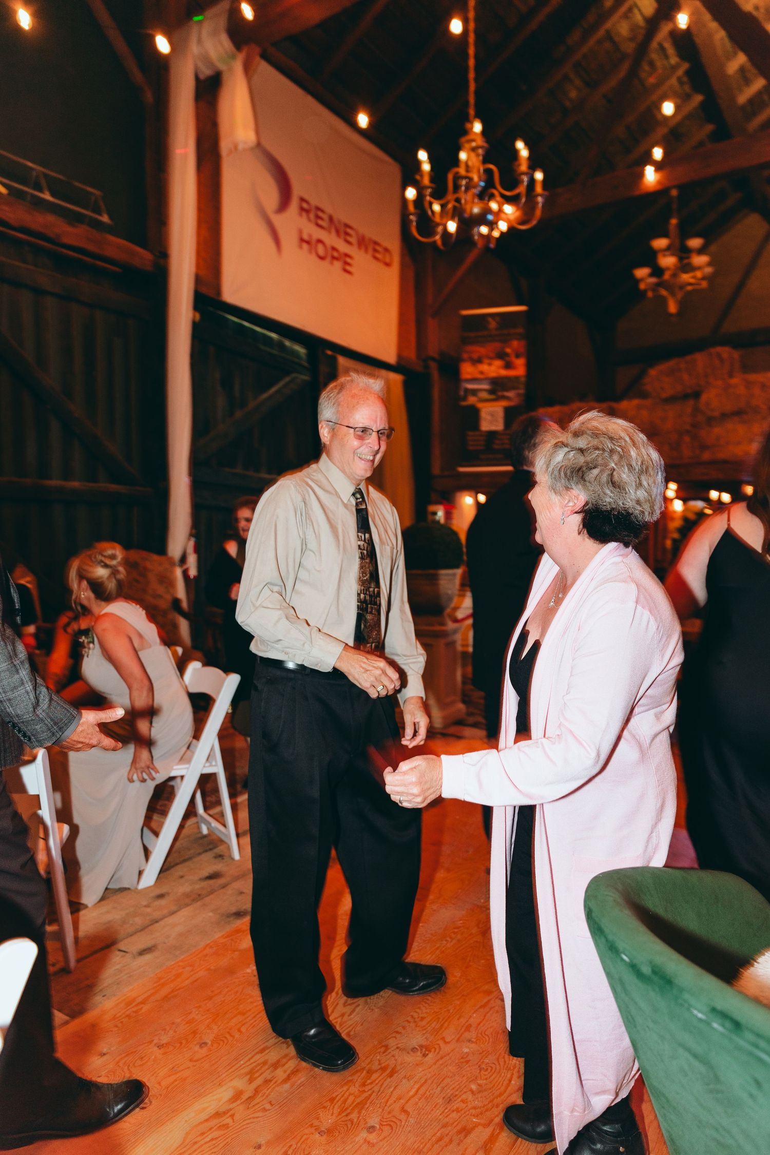 Wedding guests dancing in a dimly lit reception hall with string lights overhead.