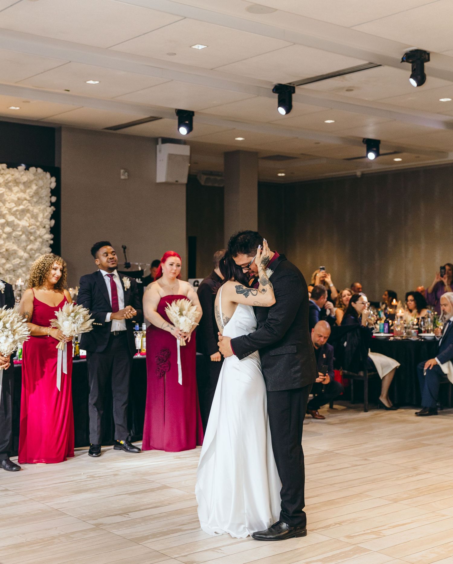 Wedding party in burgundy dresses and formal attire dancing at an elegant indoor reception.