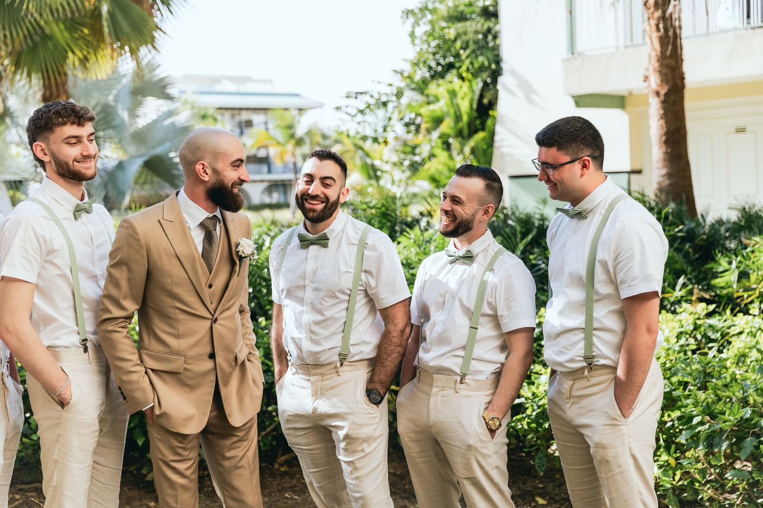 Wedding party in tan and white attire gathered outdoors under palm trees.