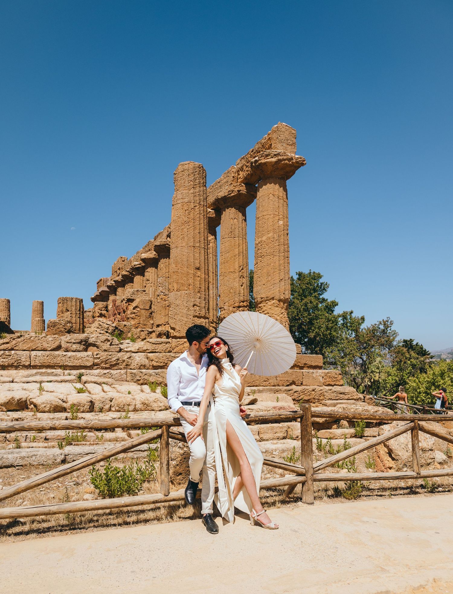 Couple with parasol creates romantic memories at ancient temple ruins under blue sky.