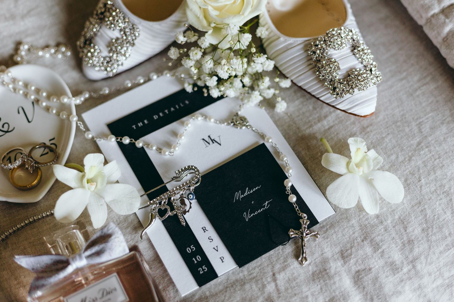 Elegant bridal accessories including white shoes, floral details and wedding stationery on textured fabric.