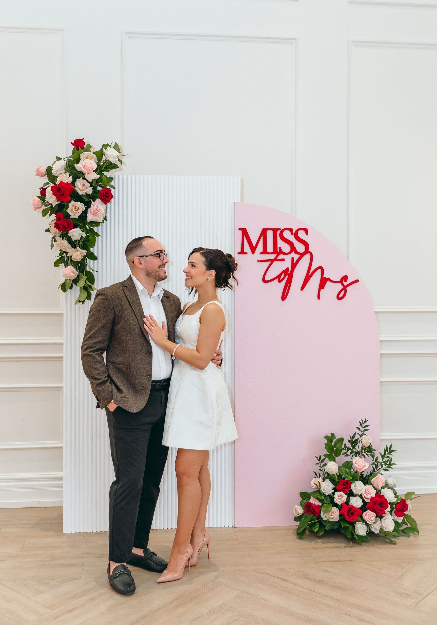 Wedding photoshoot setup with pink backdrop, white panels, and floral decorations.