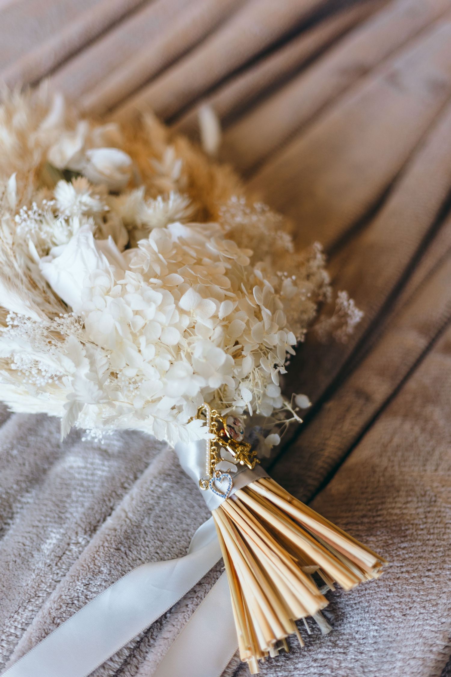 Delicate white dried flower bouquets with gold wrapping lay on wooden surfaces.