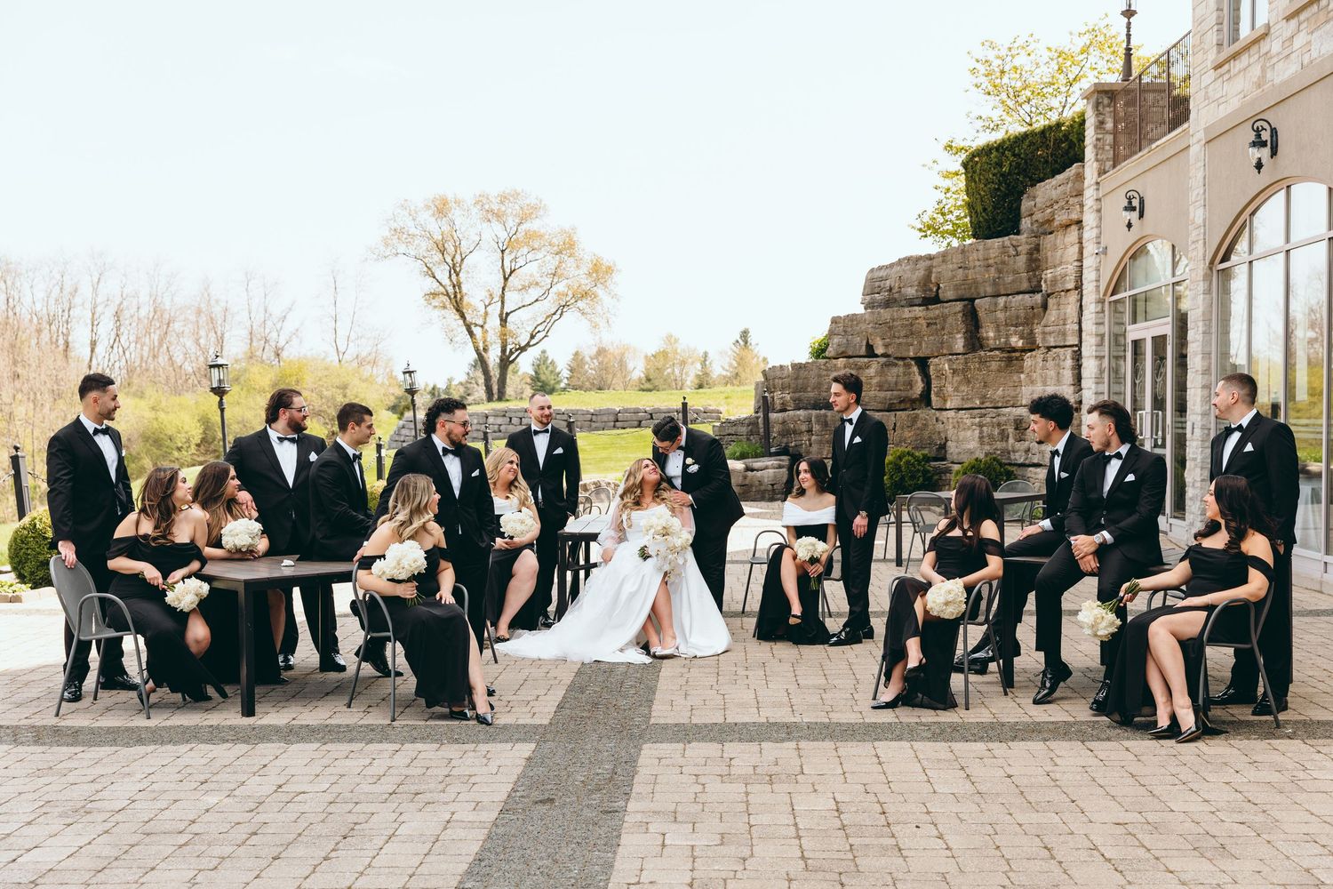 Wedding party group photo with bridesmaids and groomsmen lined up along stone wall.