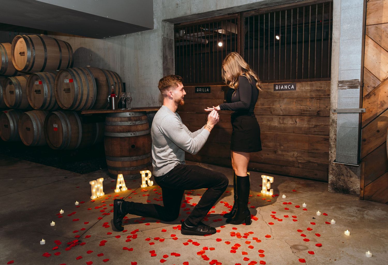 Couple sharing a romantic moment in a dimly lit wine cellar with illuminated letters in the background.