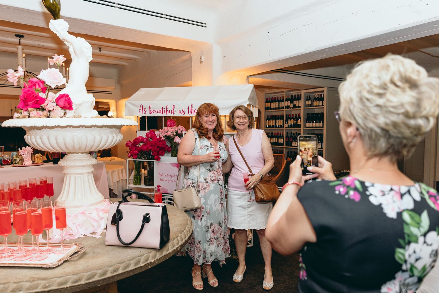 Guests mingling at an elegant event with white decor and floral arrangements visible in the background.