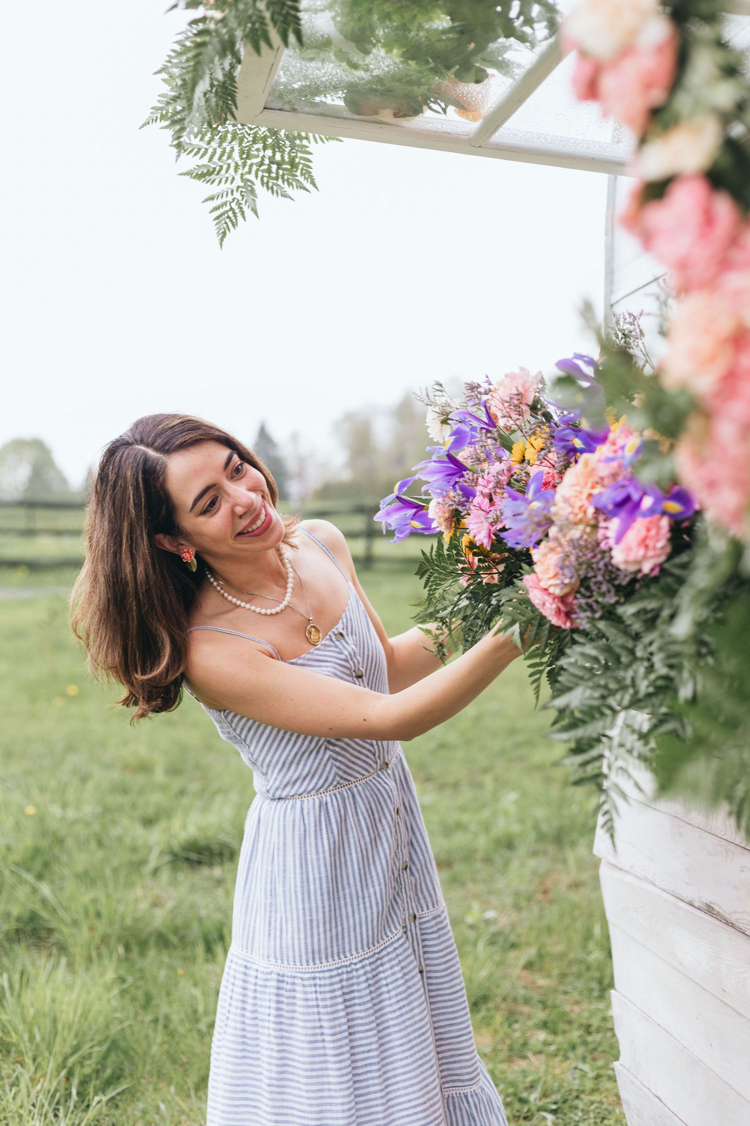 Woman in striped summer dress joyfully arranges colorful flowers in an outdoor garden setting.