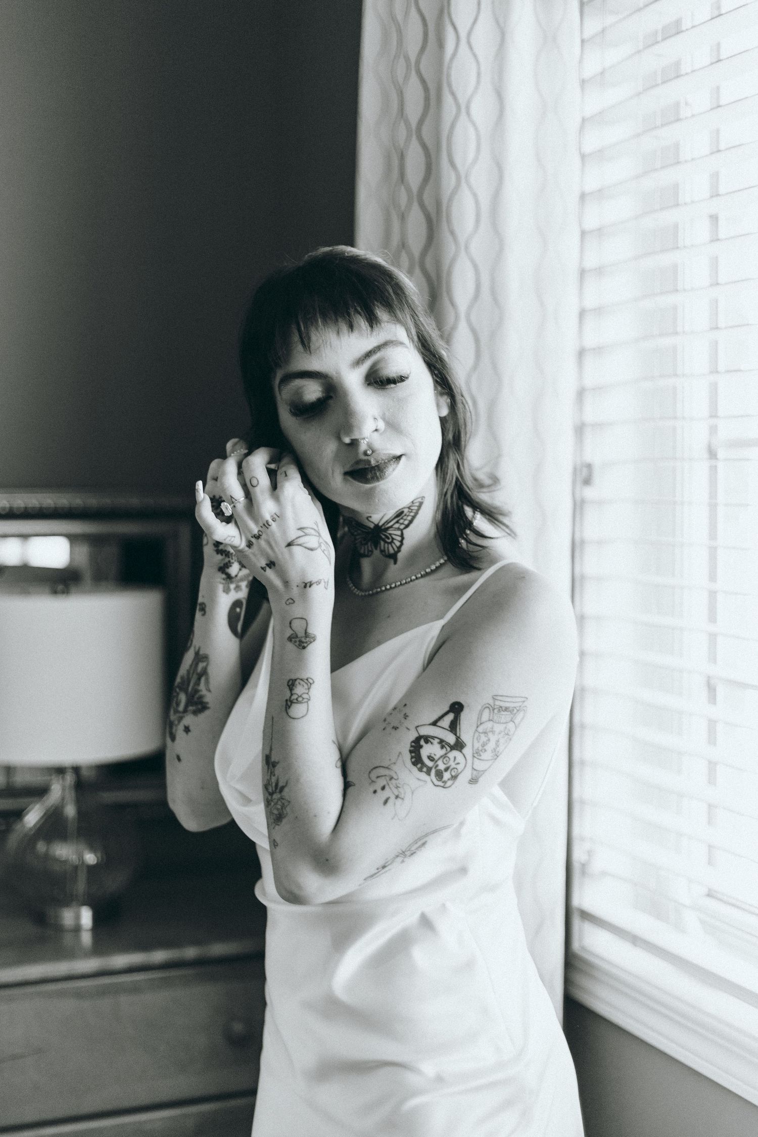 Black and white photos of someone in a white top posing playfully near a window.