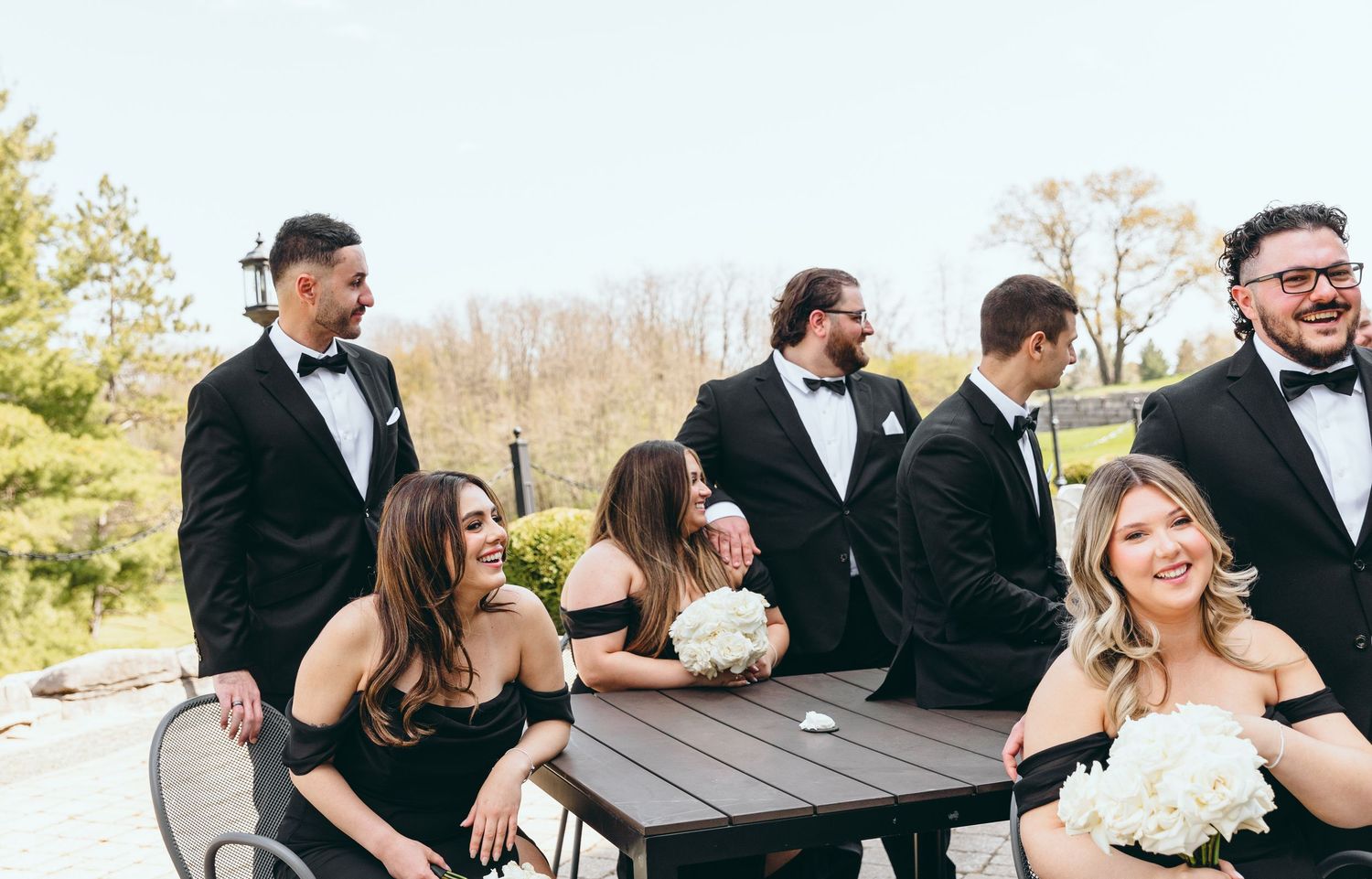 Wedding party relaxes and laughs together at outdoor tables.