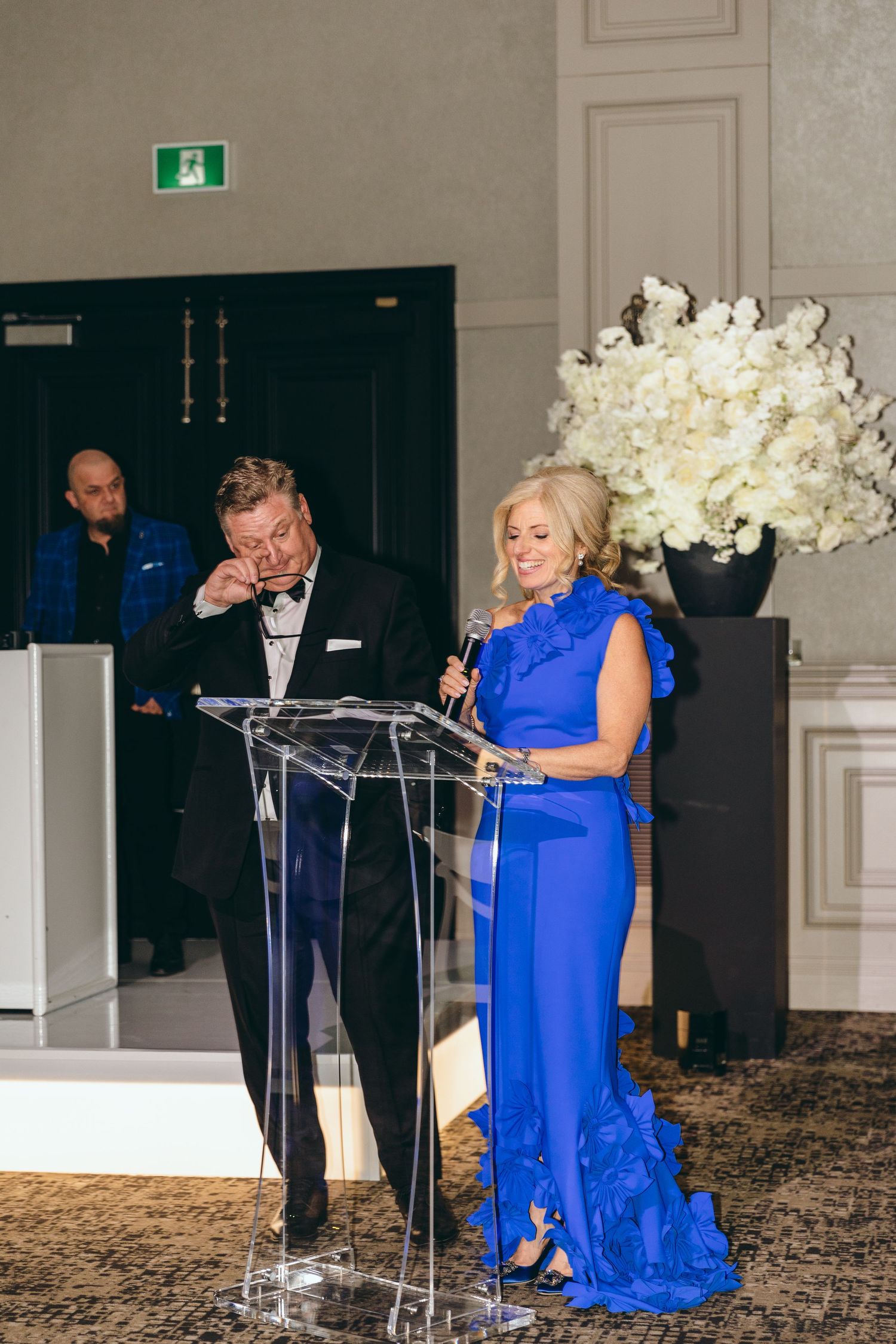 Formal event speakers at a podium with elegant white floral arrangements and decor.