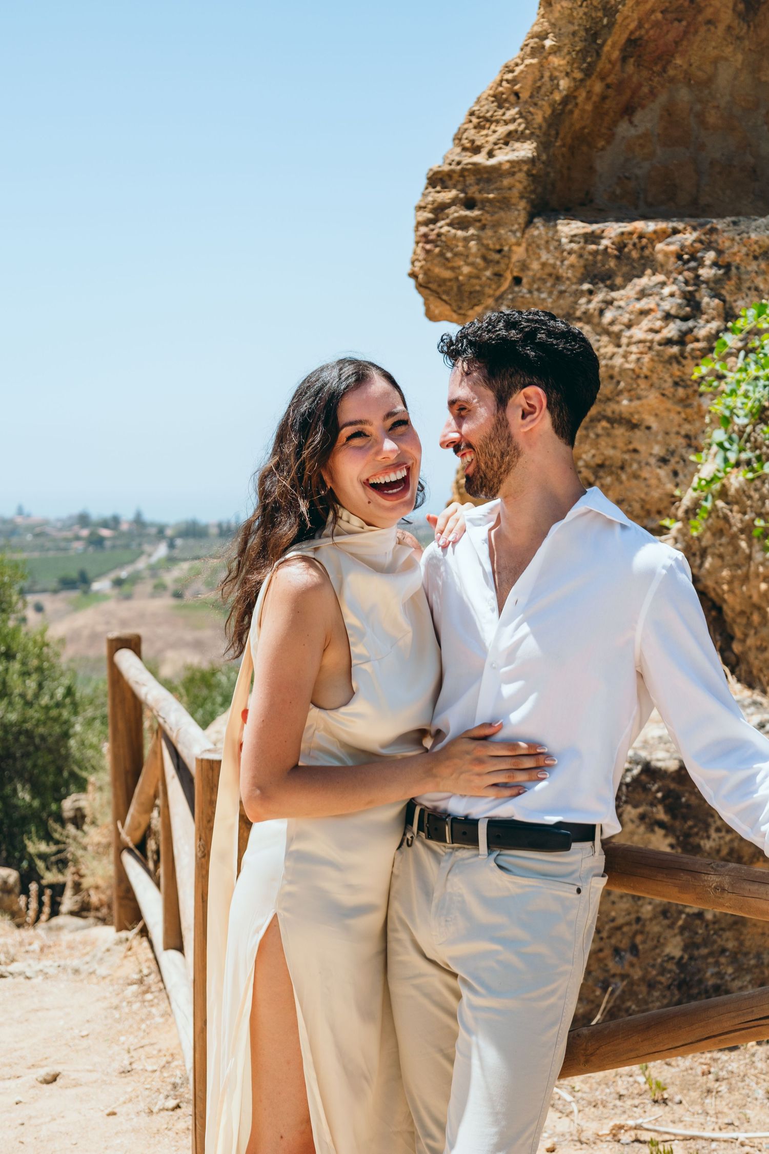 A joyful moment captured between a couple in white outfits against a natural landscape.
