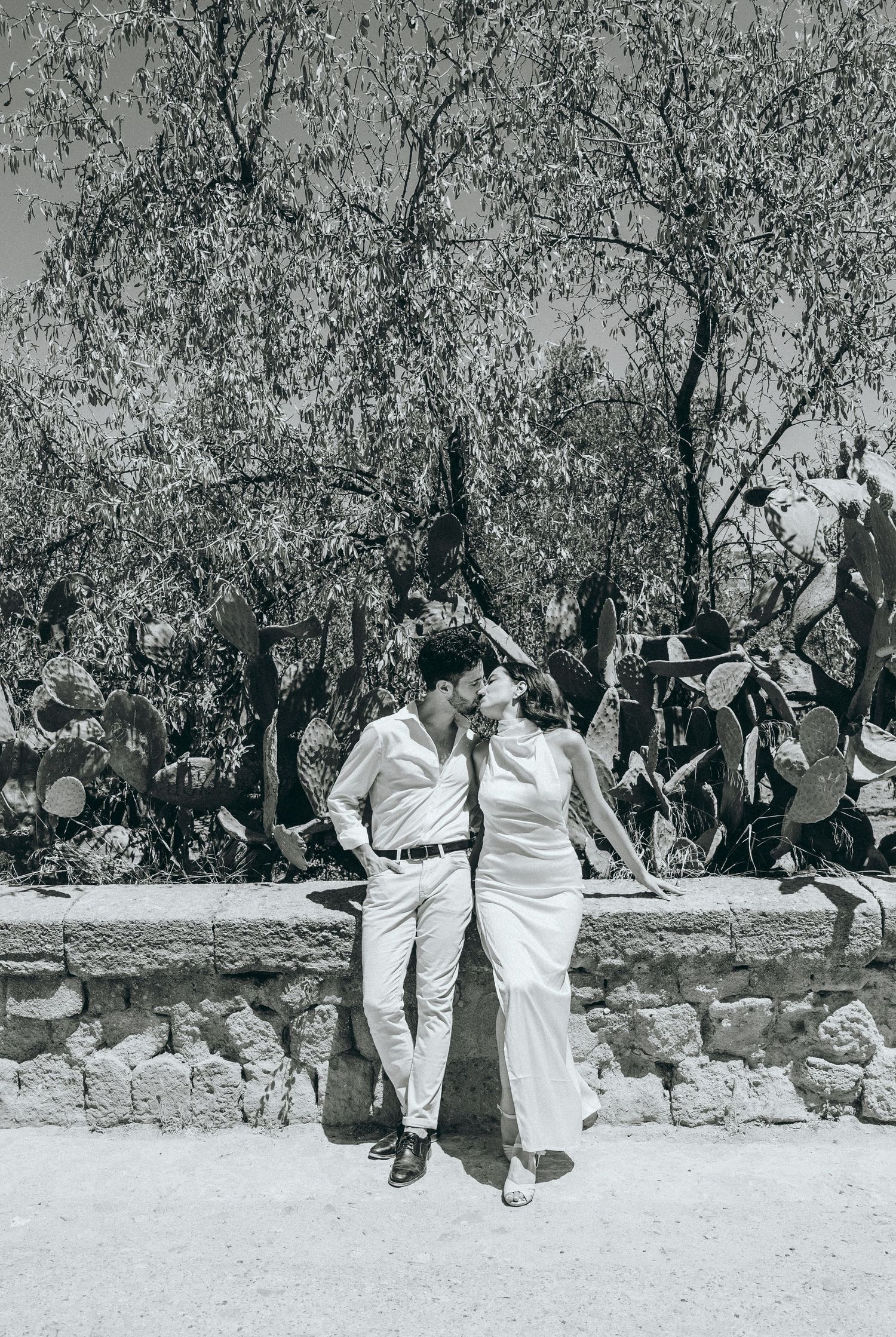 Black and white photo series showing playful moments between couple near stone wall.