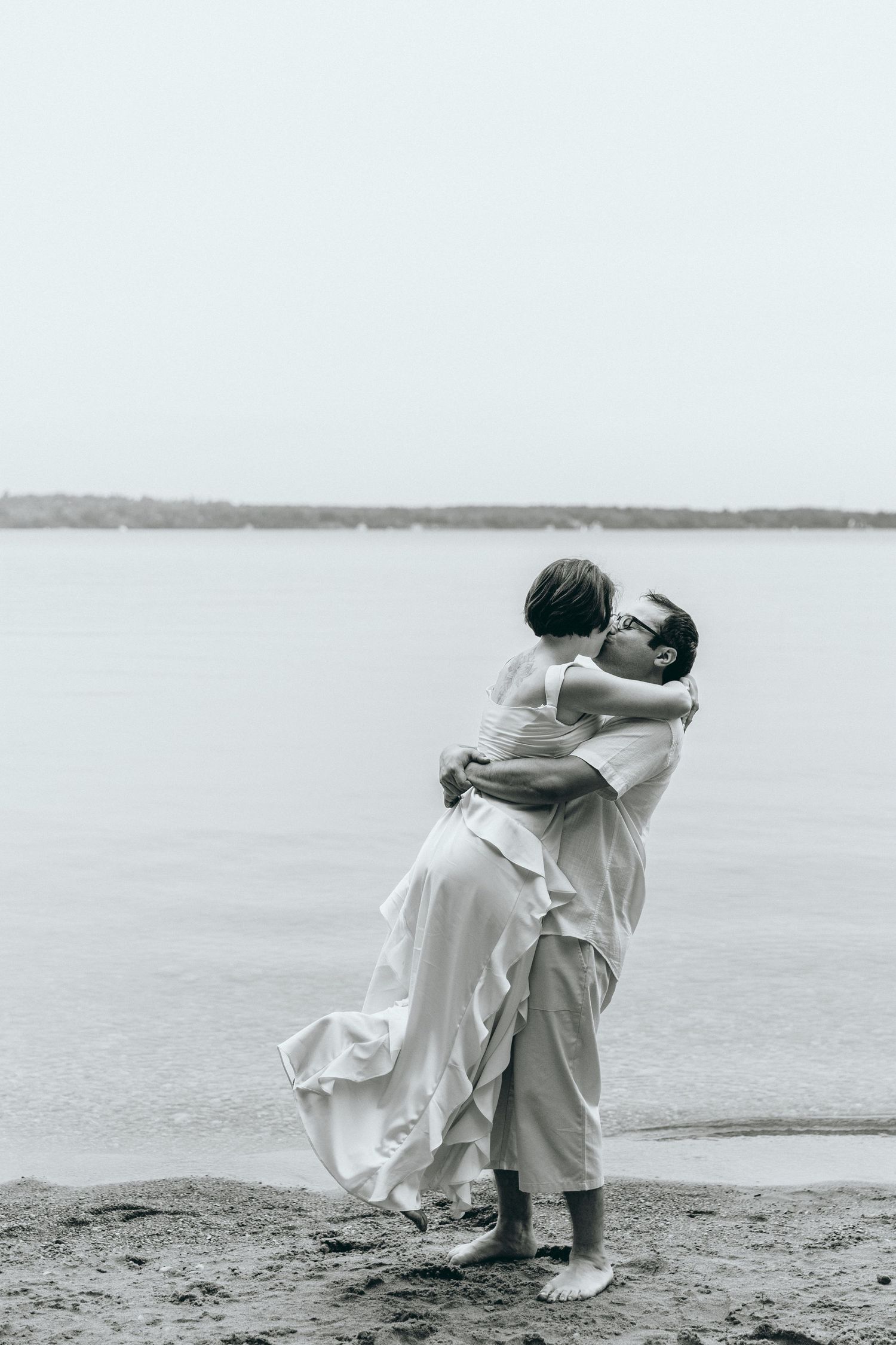 Two people sharing an intimate dance moment on a beach in white attire.
