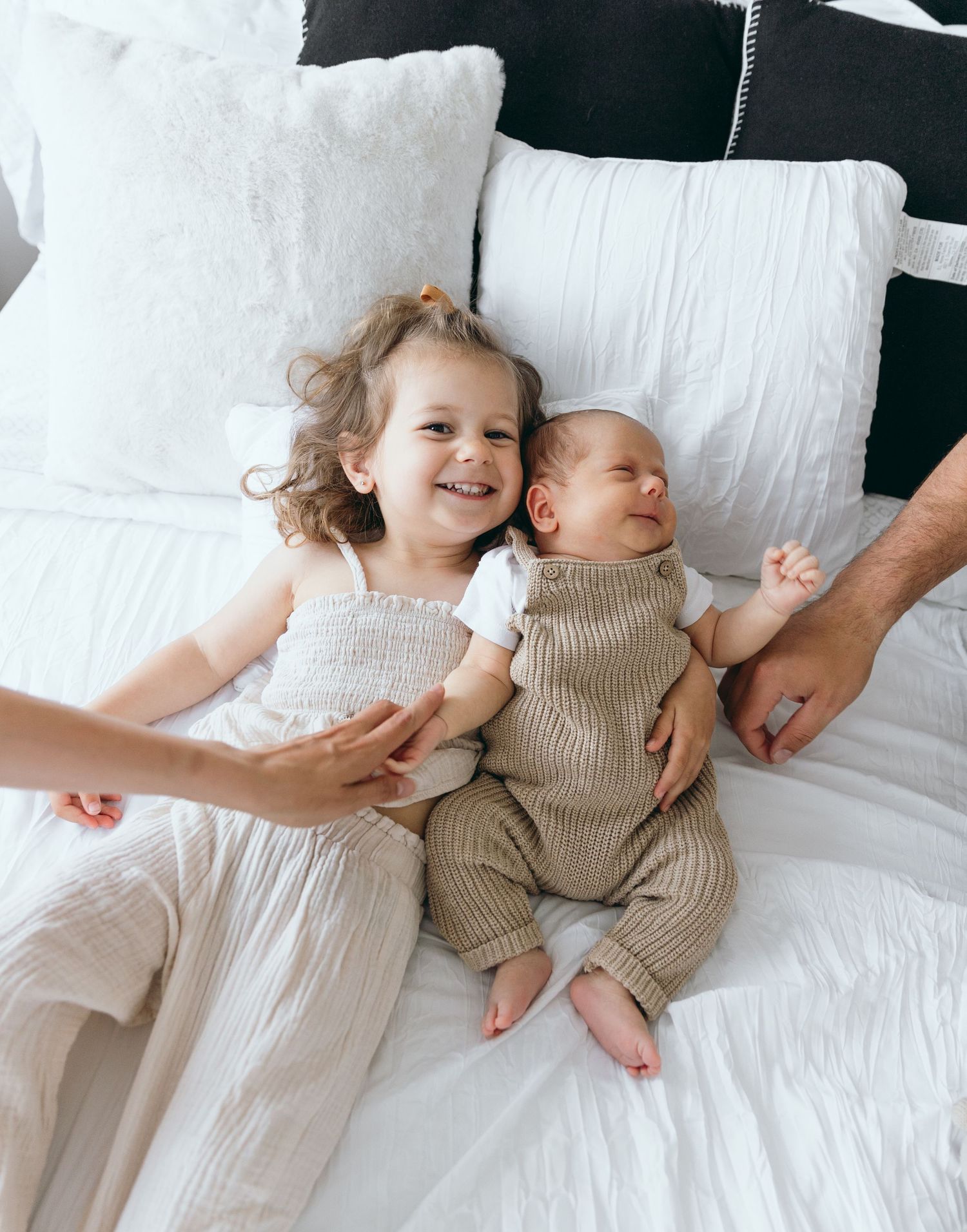 Two children rest peacefully on white bedding wearing contrasting light and beige outfits.