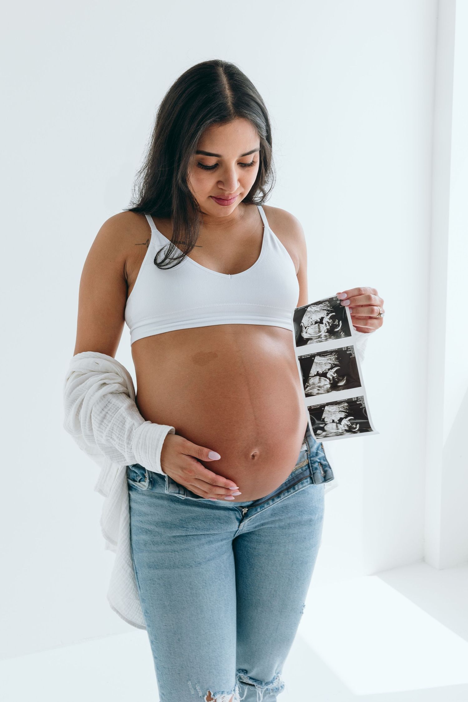 Expectant mother holds ultrasound photos during minimalist studio maternity session.