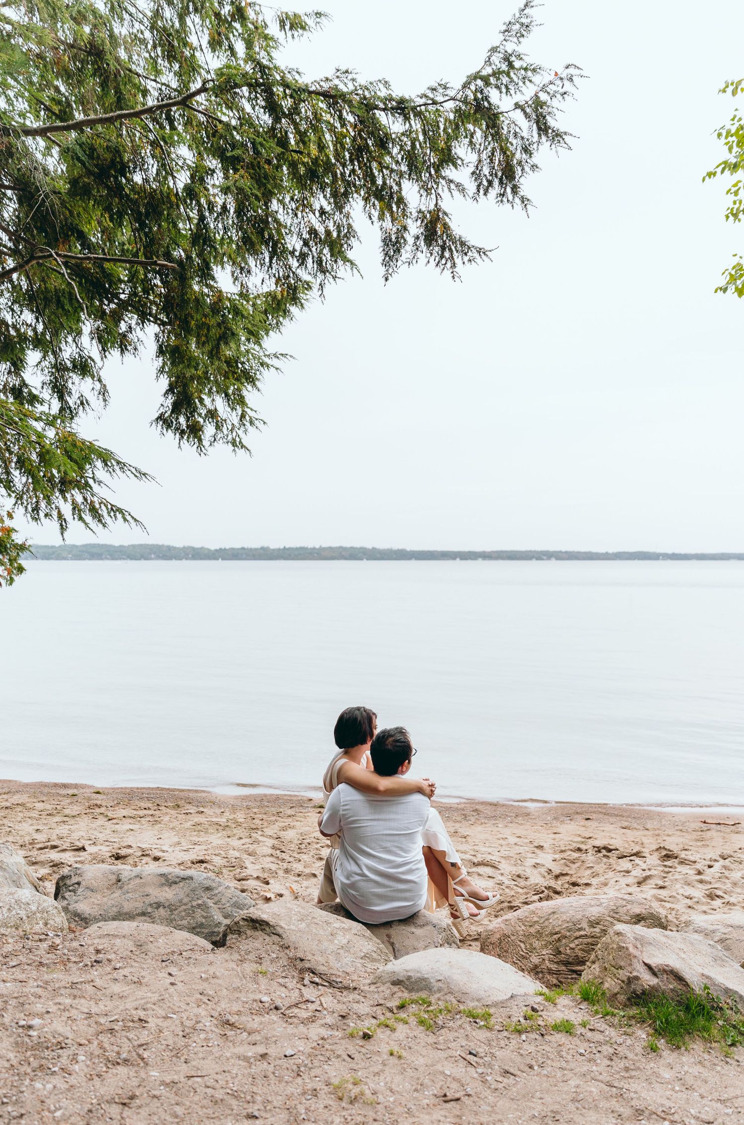 Romantic beach scene with couple sitting on rocky shore by the water.