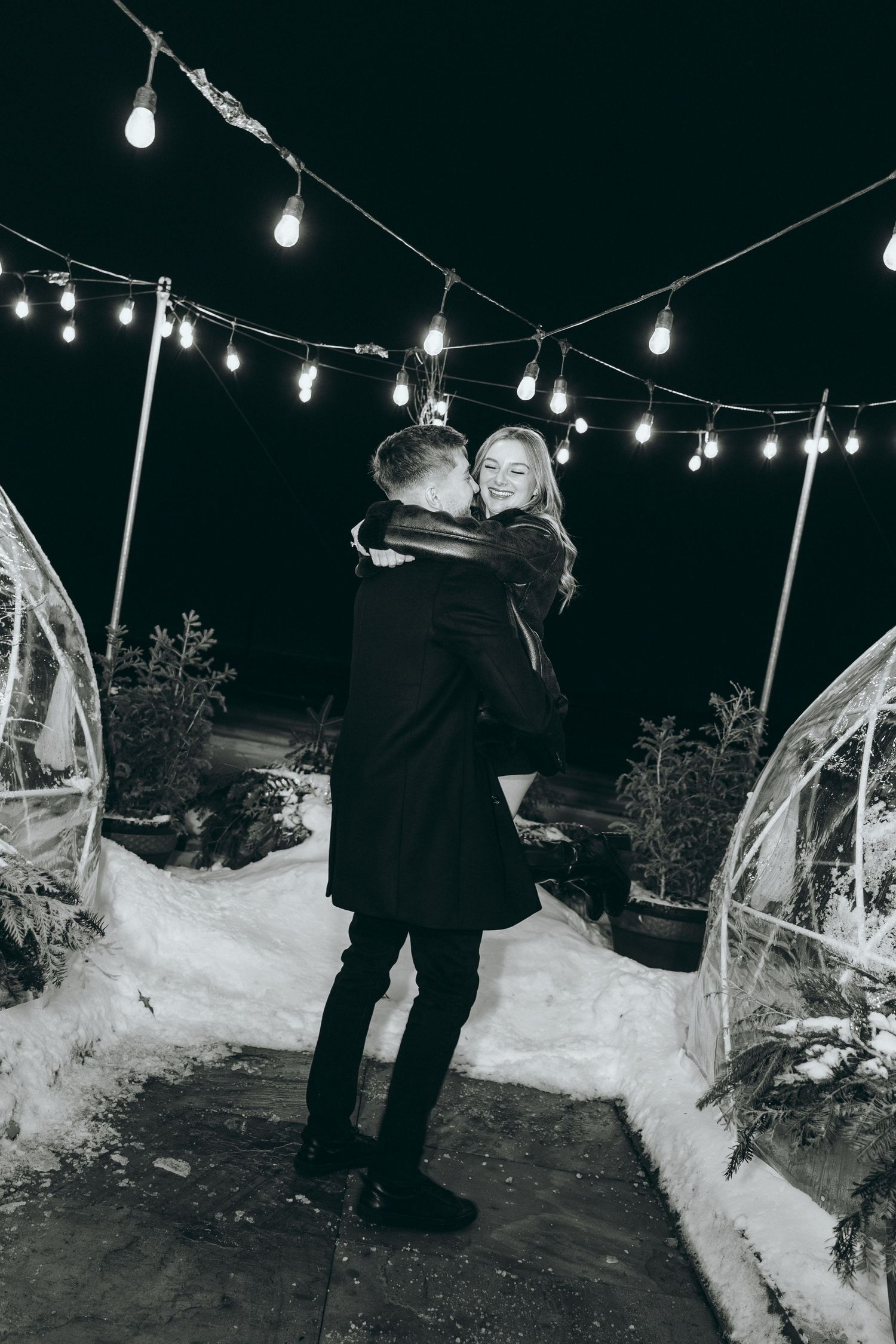 Nighttime winter scene with string lights and snow showing romantic moment.
